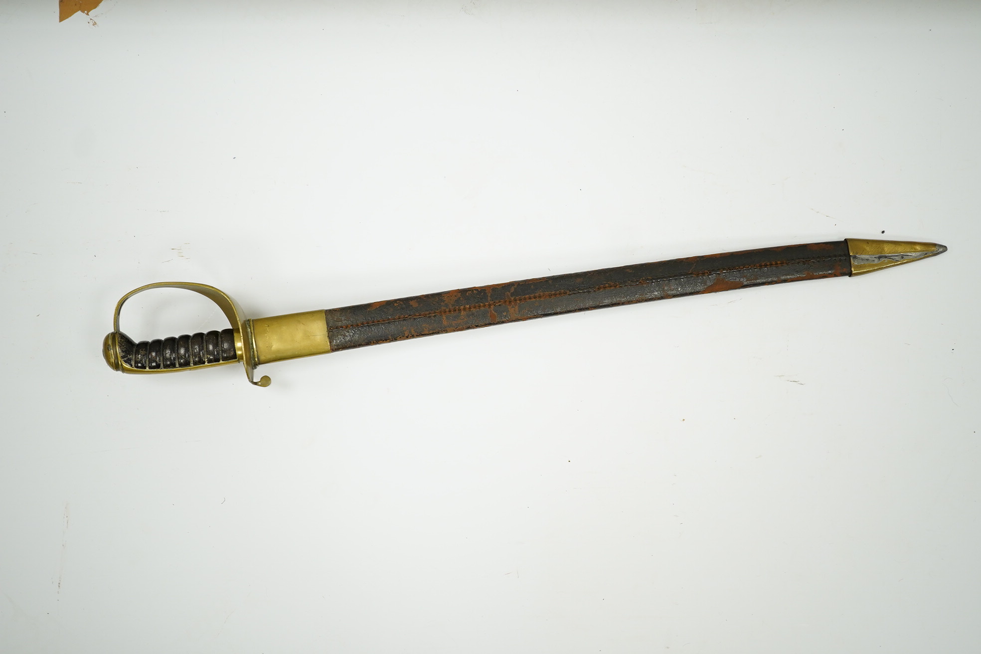 A late 19th century boarding cutlass with plain blade, plain brass guards and mounts, and leather covered grip, in its brass mounted leather scabbard (the chape is an associated replacement). Condition - fair